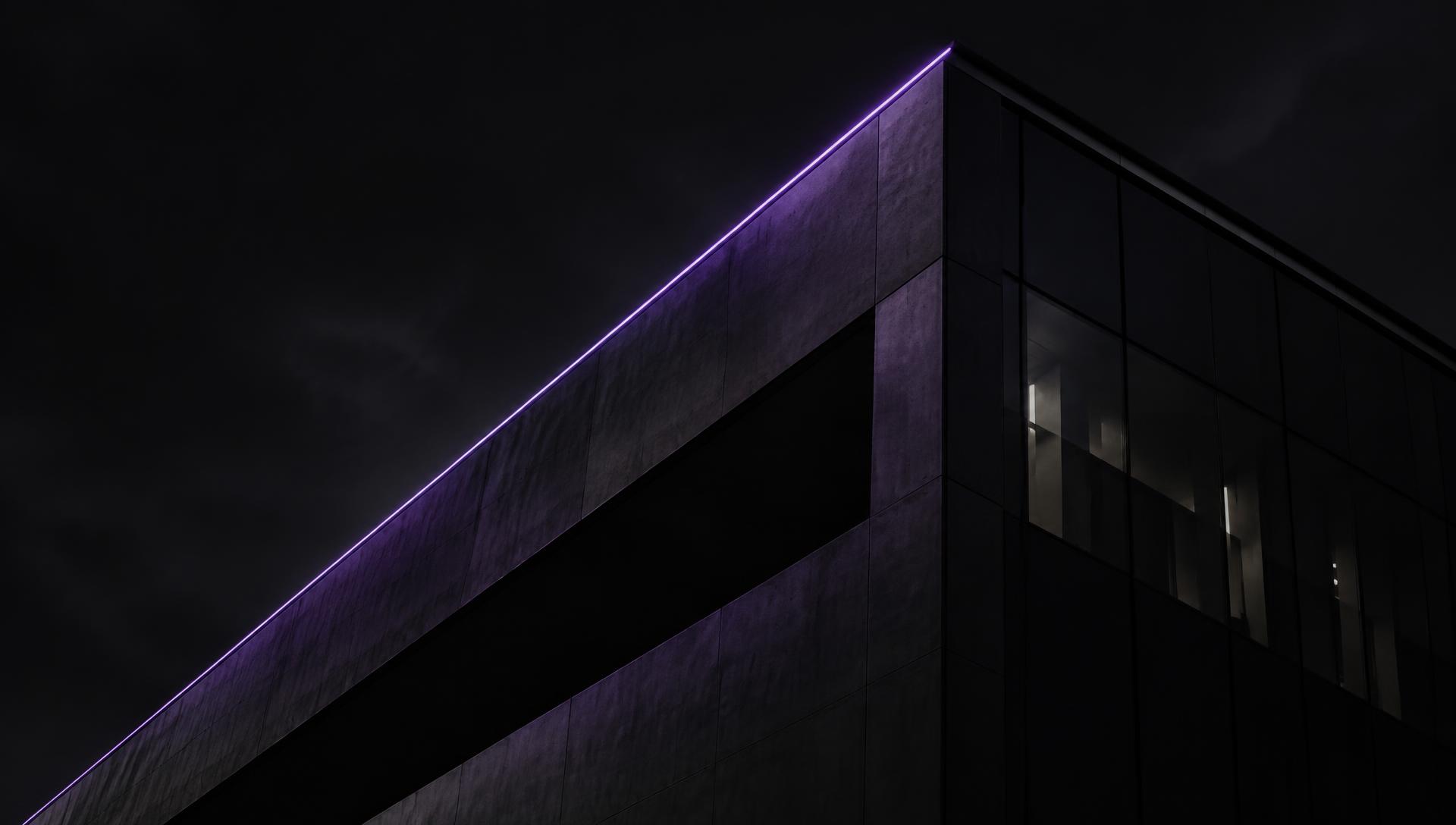 Modern building facade at night outlined by a thin line of purple light